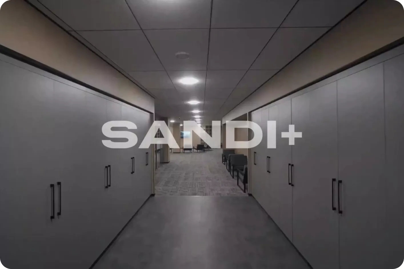 Sandi+ logo projected at the end of a dark office corridor